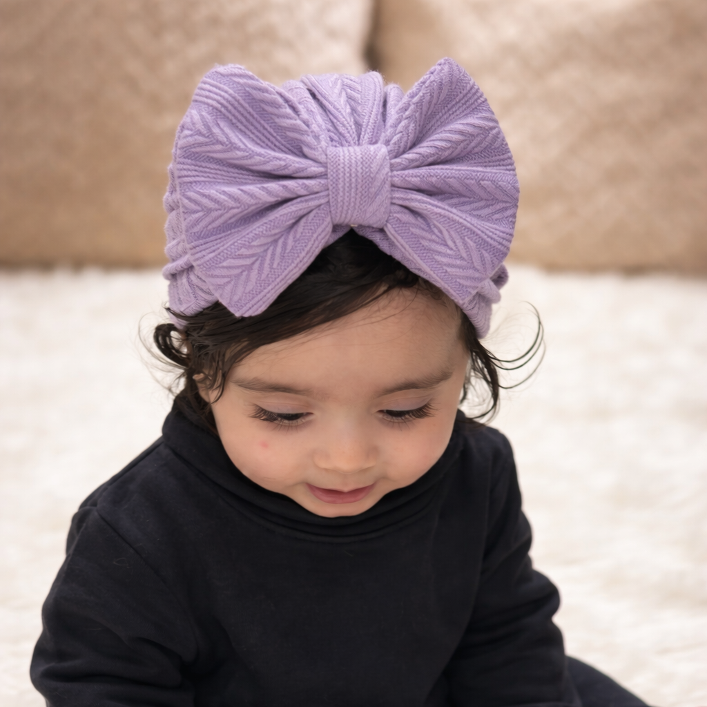 Child wearing a black outfit and purple headband sitting on a white surface.