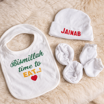 Baby bib, hat, and booties with personalized name on a soft surface