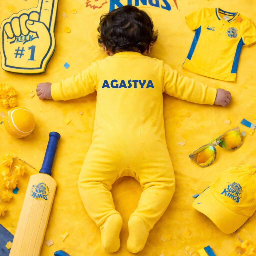 Baby in a yellow outfit with 'Chennai Super Kings' branding surrounded by sports-themed items on a yellow background.