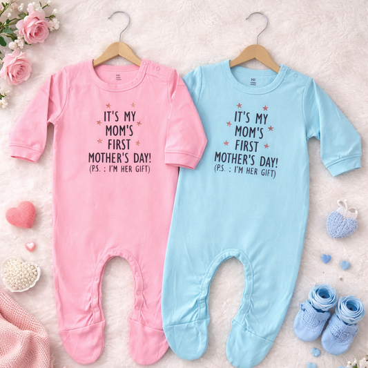Two baby onesies, one pink and one blue, with text on hangers on a soft surface with decorative items.
